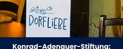 Beitragsbild Dorfliebe-Tour in Beuna Das Plakat der Dorfliebe-Tour hinter einem kleinen, runden Esstisch