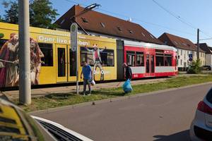 zwei Bürger sammeln Müll an einer Straßenbahnhaltestelle, im Hintergrund die Straßenbahn